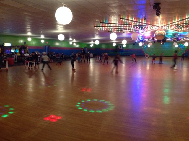 Skaters and colorful disco lights reflected on Skateville’s wooden floor